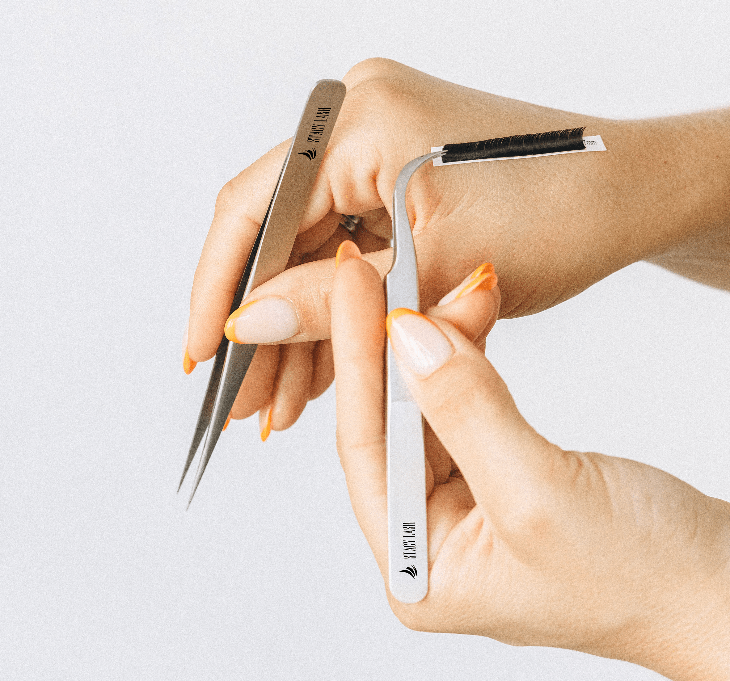 2 pairs of tweezers in both hands holding lashes on a strip